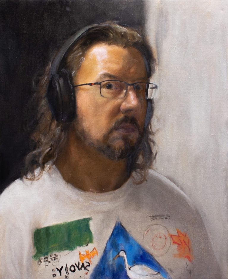 Middle aged man with long, shoulder length brown hair. Looking directly at the viewer, wearing noise cancelling headphones and a Basquiat T-shirt